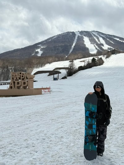 Mia stands with a snowboard ahead of the Appi Kogen welcome sign.