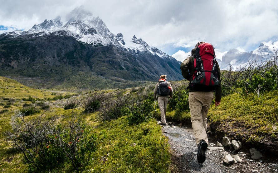 couple hiking up mountain with snow-capped peaks in the distance