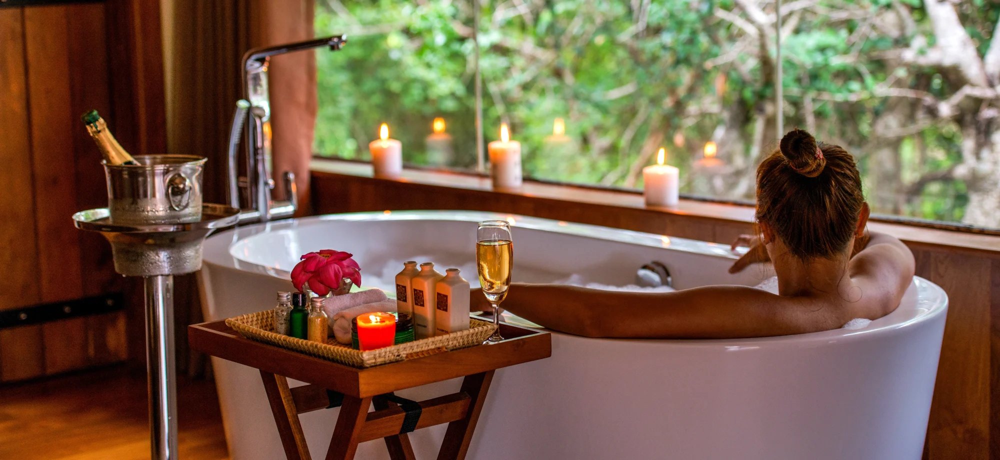 A woman is sitting in a bathtub with champagne and a candle. 
