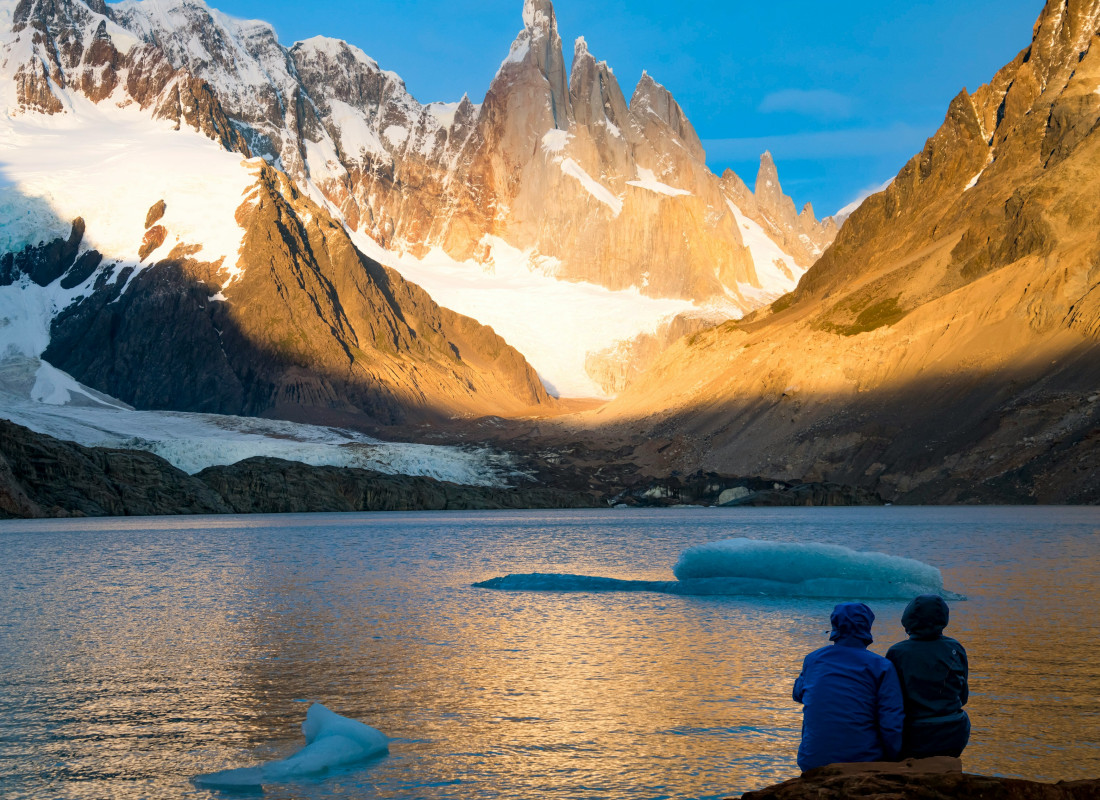 Two people sit on a rock looking out to the massive snow-capped hills of Glaciares National Park.