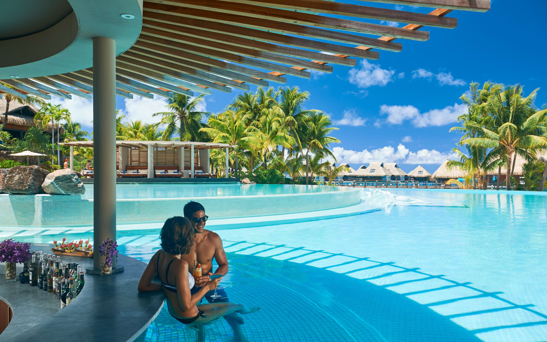 A couple are sitting on stools in water at the pool bar. 