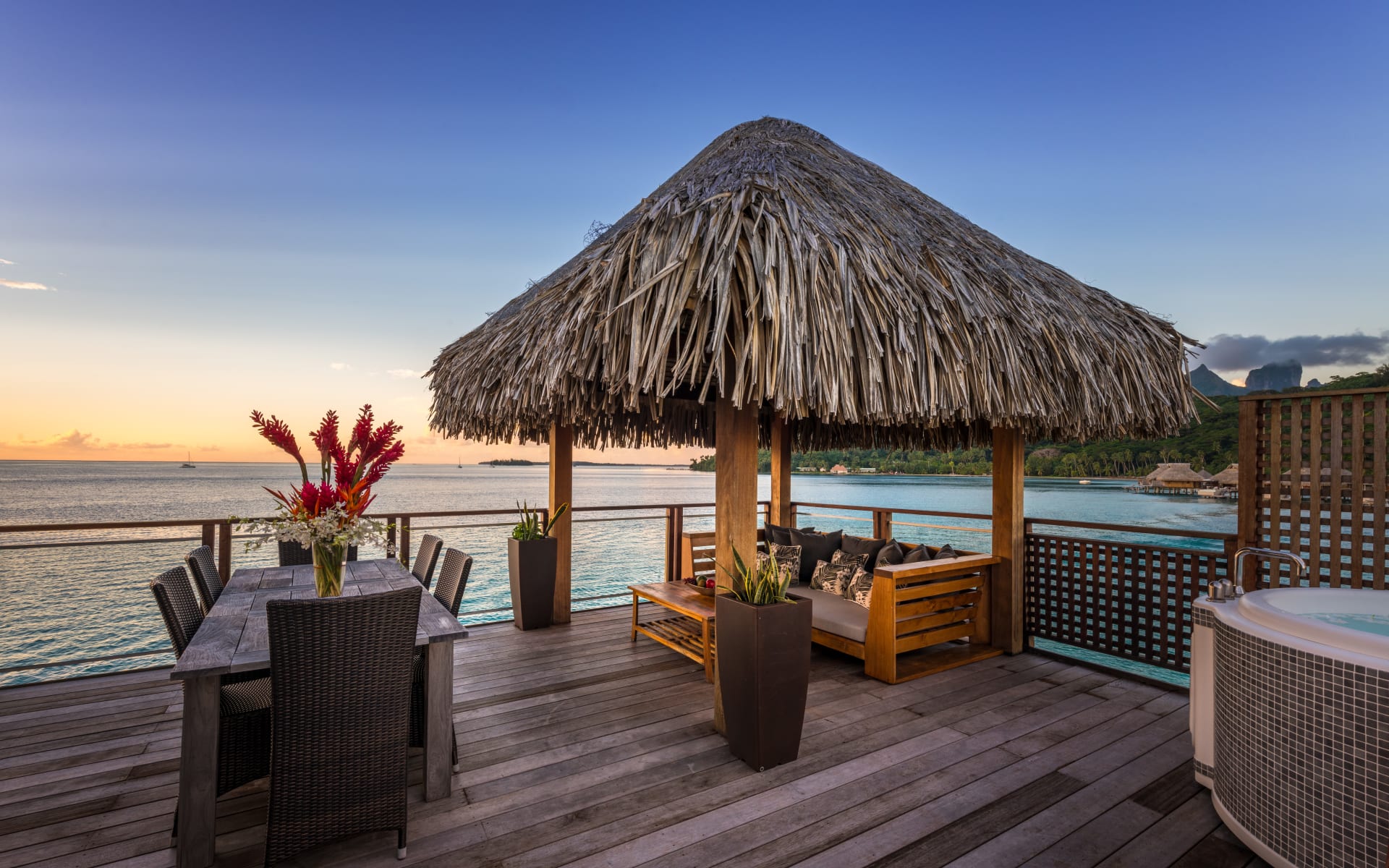 There is a table and seating area under a thatch-roof, overlooking the sea. 