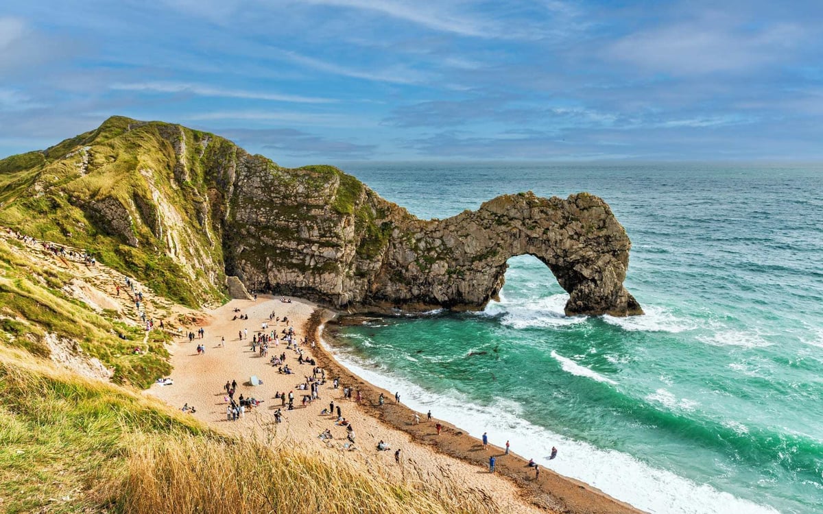 This beach on the Jurassic Coast has golden sands and is busy, with a door-shaped geological formation edging into the sea.