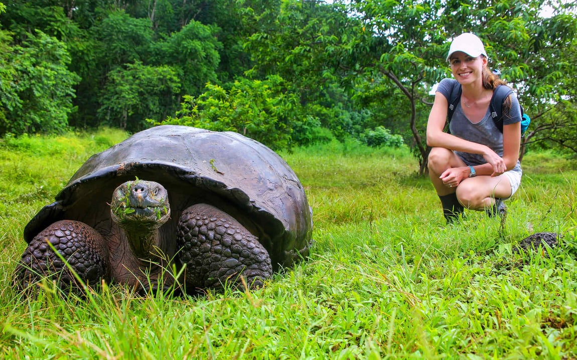 A lady sits beside a giant tortoise in the Galapagos Islands.
