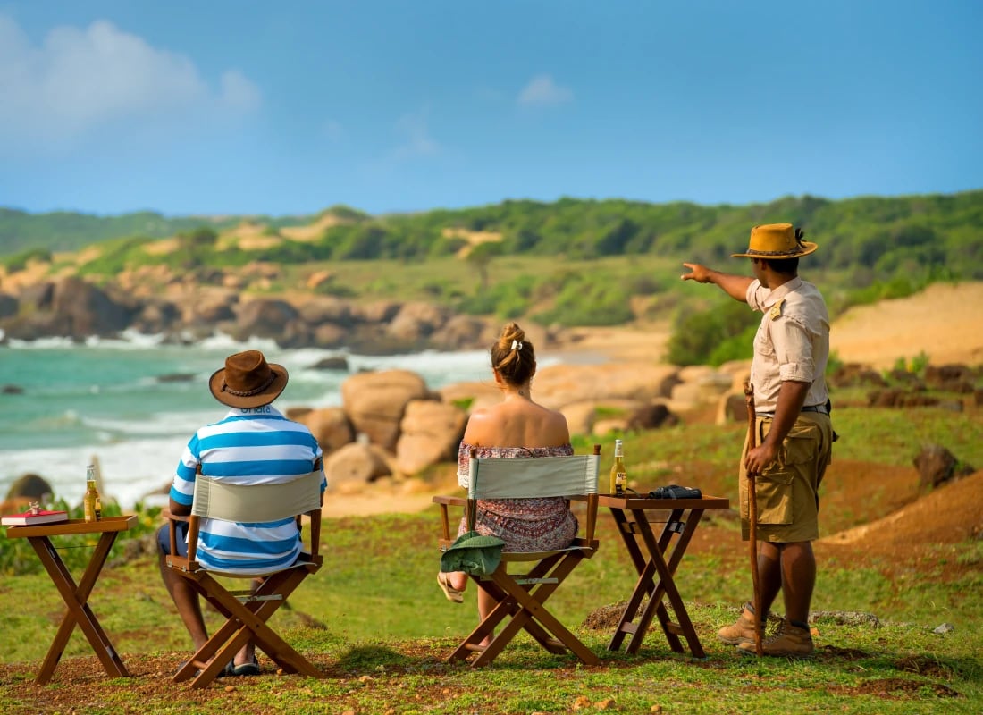 Two people are sitting on chairs, looking at the ocean. 