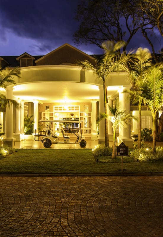 The exterior front entrance to the hotel is lit up during a clear evening. Palm trees surround the entrance.
