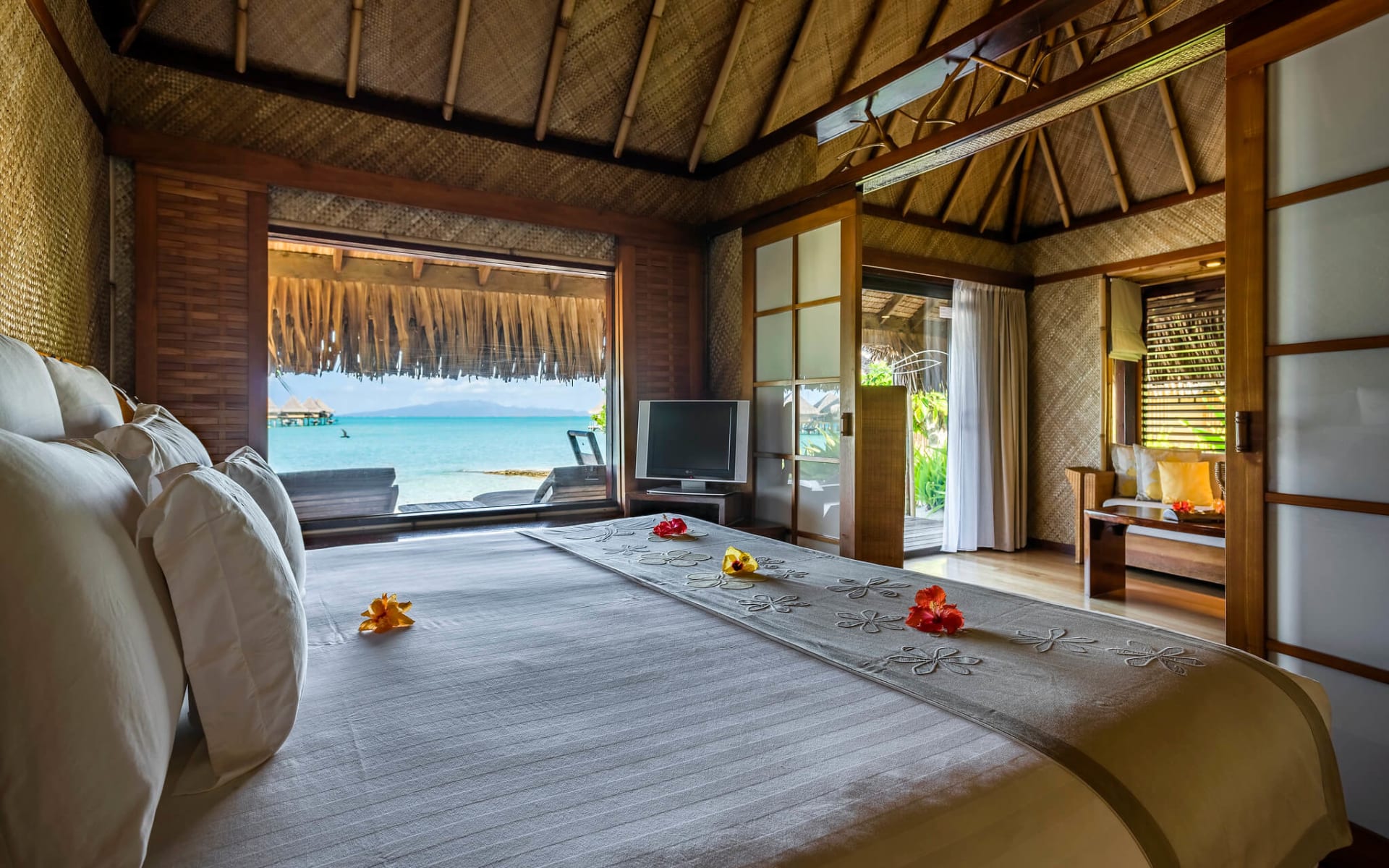 A double bed has flowers on it and the room opens to a balcony. 