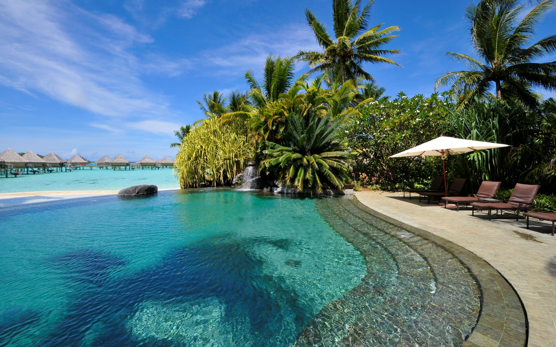 A swimming pool has sunloungers and a white umbrella. 