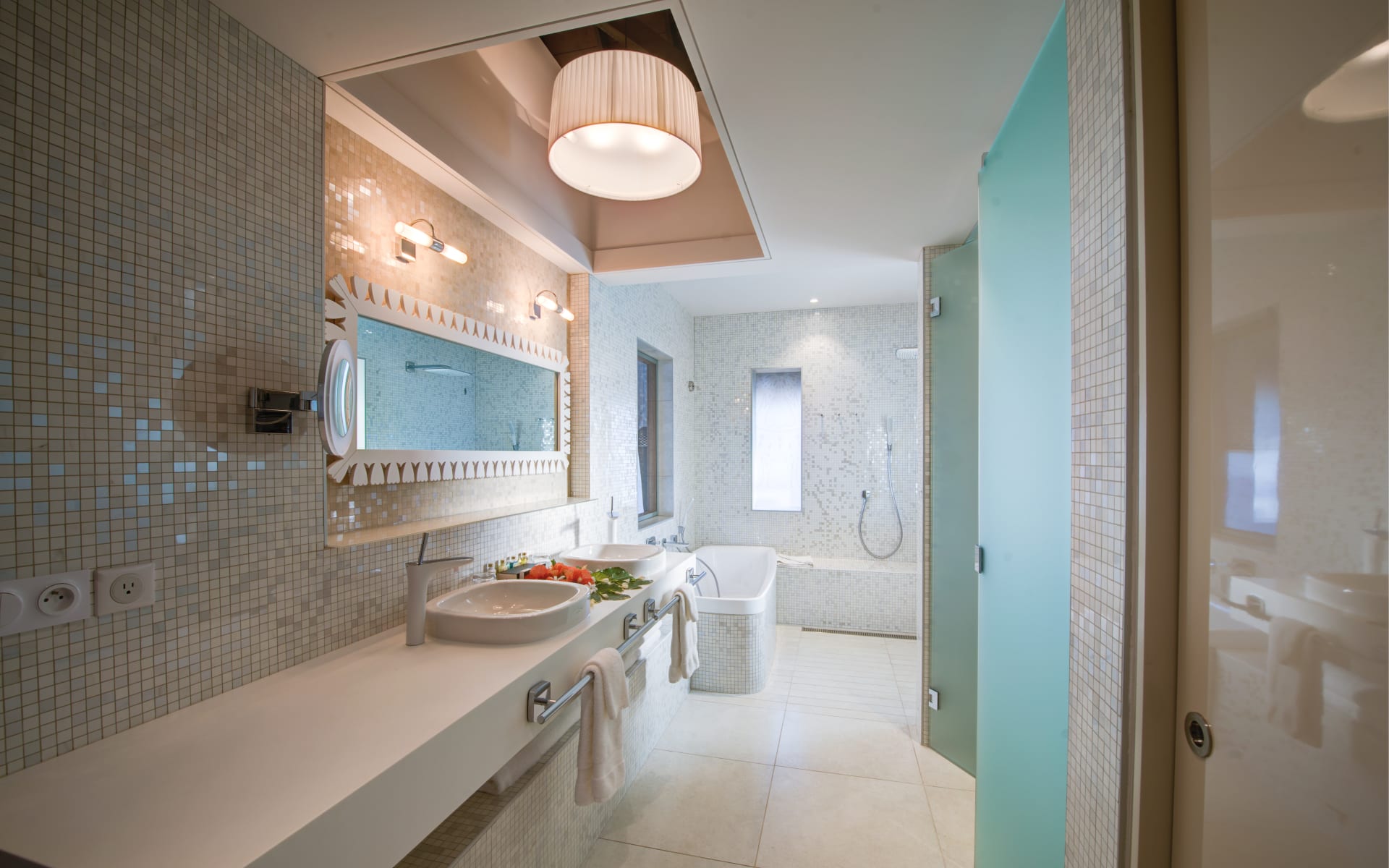 A marble bathroom has a long sink and rainfall shower.