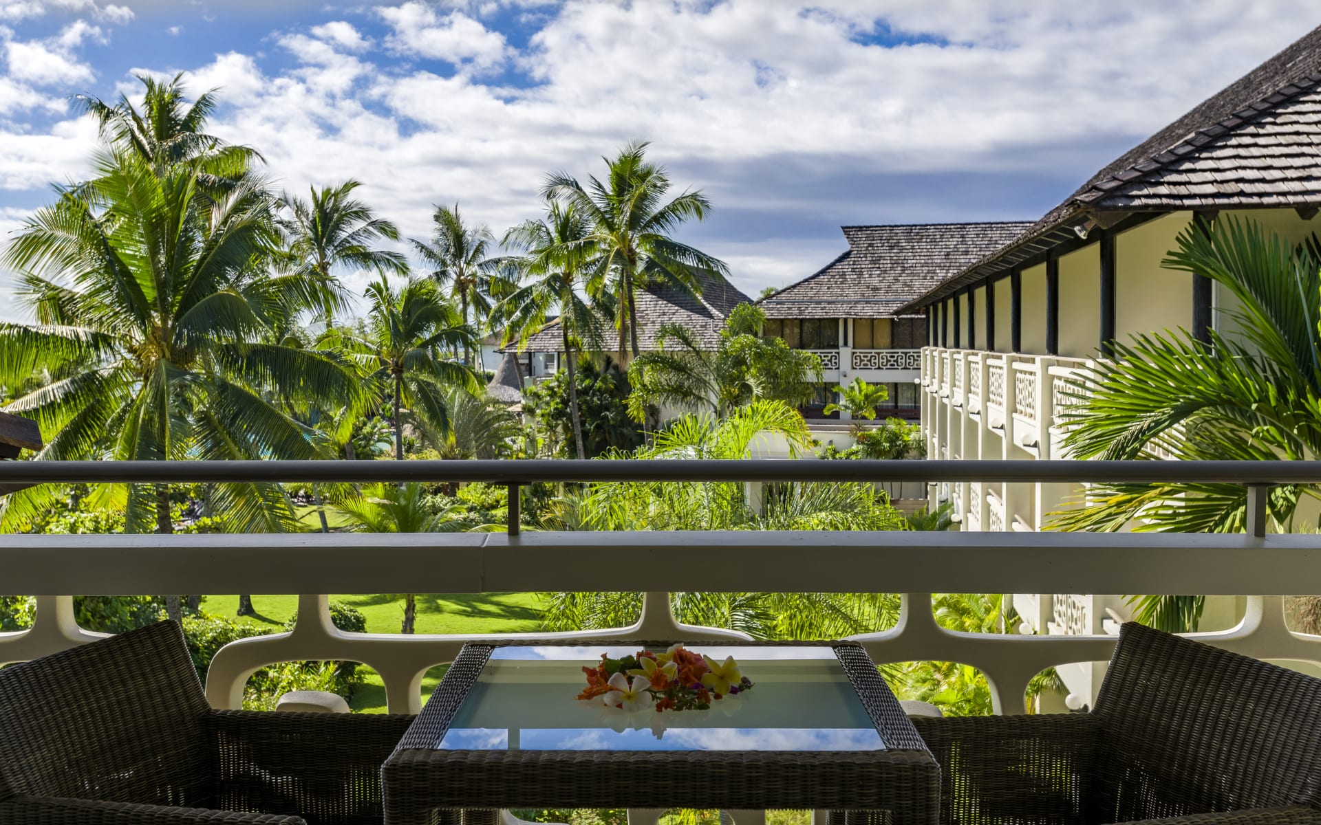 A balcony has a table and chairs overlooking the garden with palm trees. 