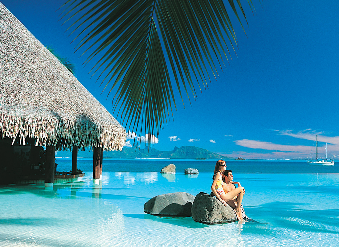 A couple are sitting on a rock in an infinity pool. 