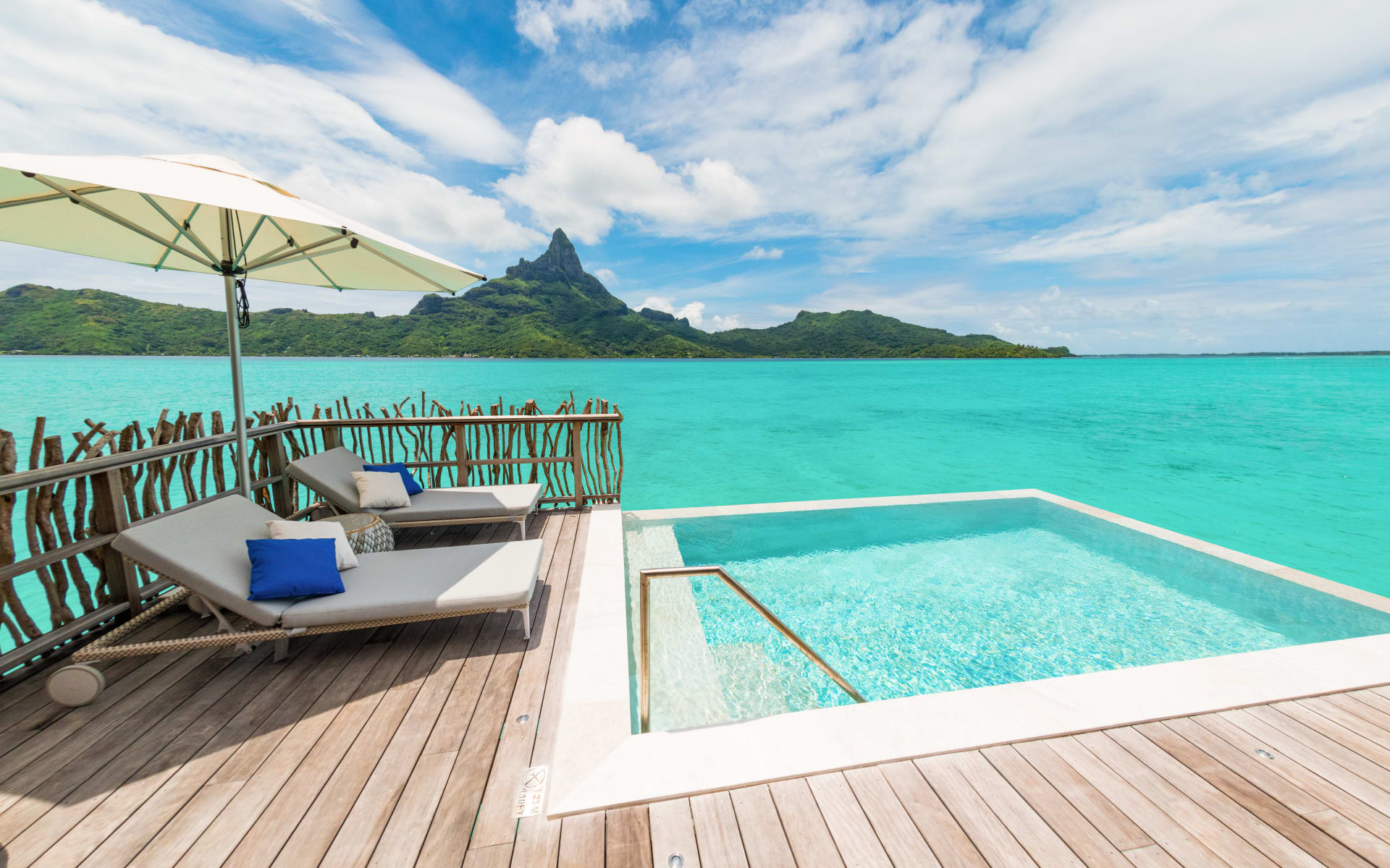 A wooden deck, hanging over the ocean, has sun loungers and a pool. 