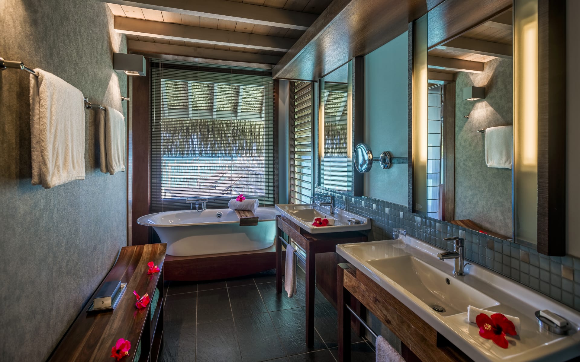 The bathroom has two sinks, a rolltop bathtub and flowers. 