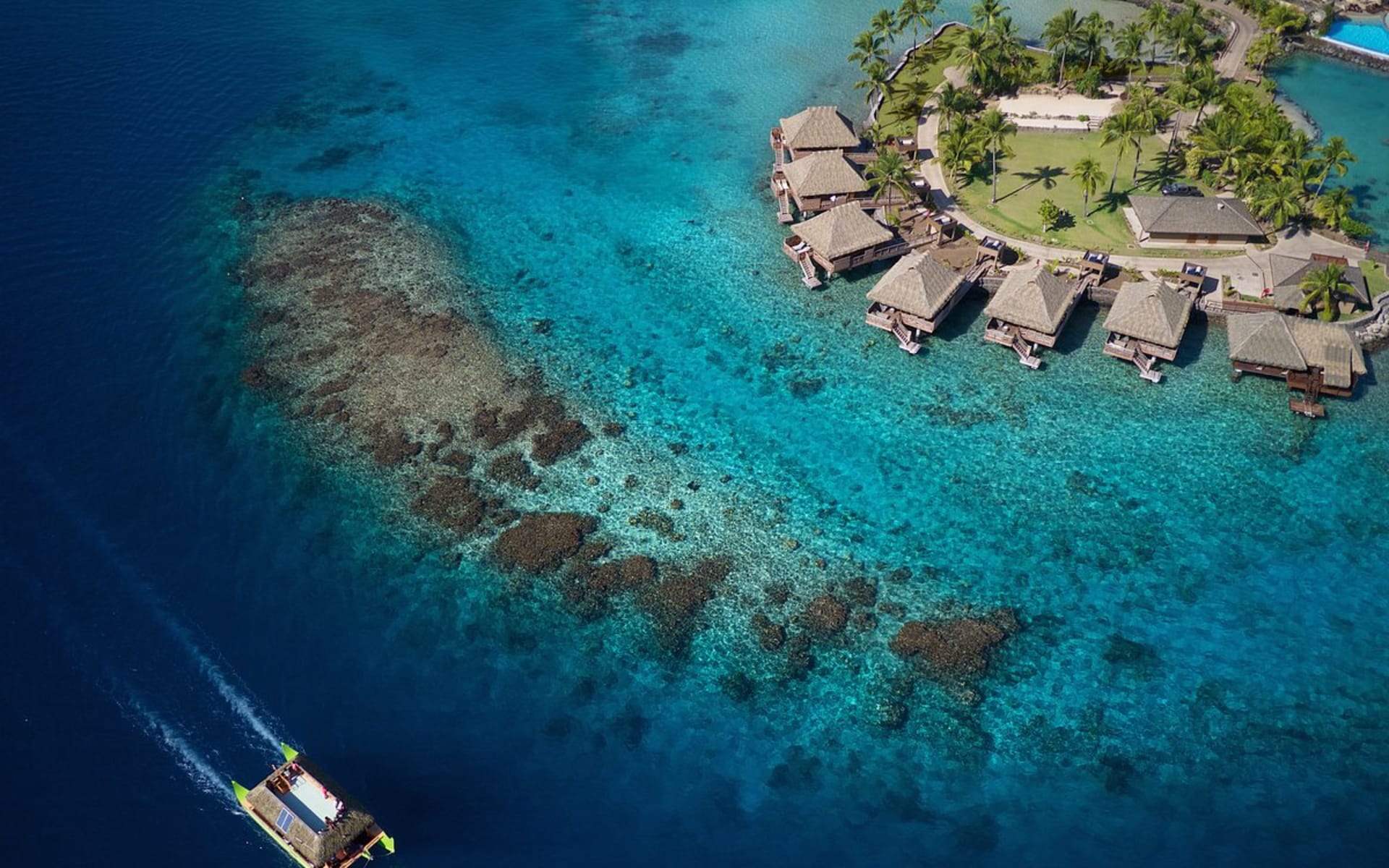 A boat is speeding past overwater villas. 
