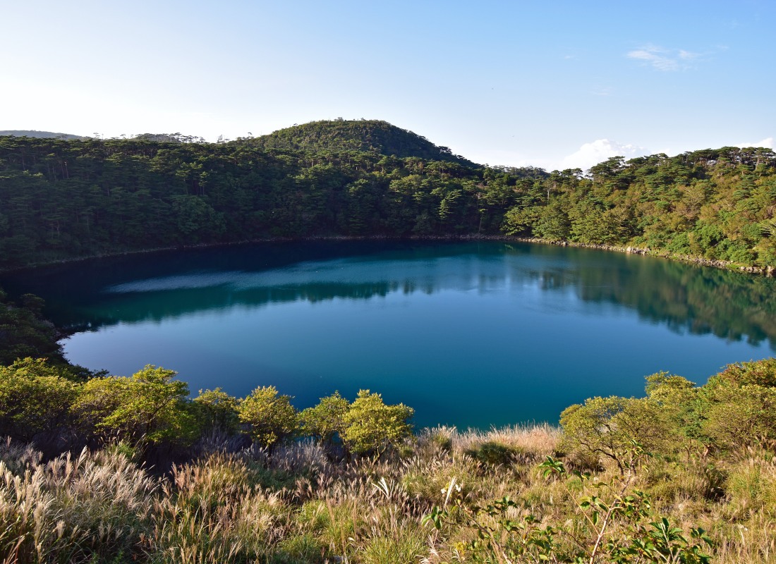 Kyushu Lake is glistening and blue, surrounded by trees and shrubbery. 