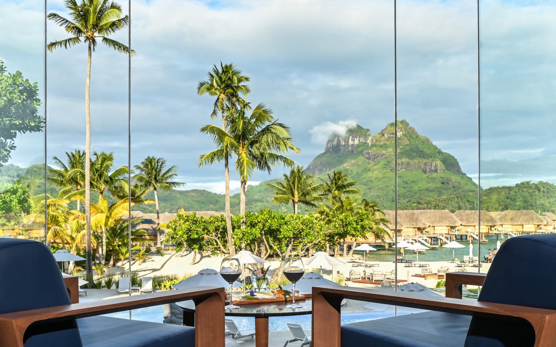 Two chairs overlook the pool, palm trees and mountains. 