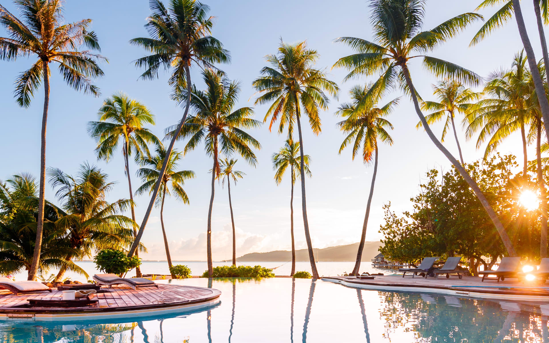 Sunset reflecting off of swimming pool with ocean and palm tree view