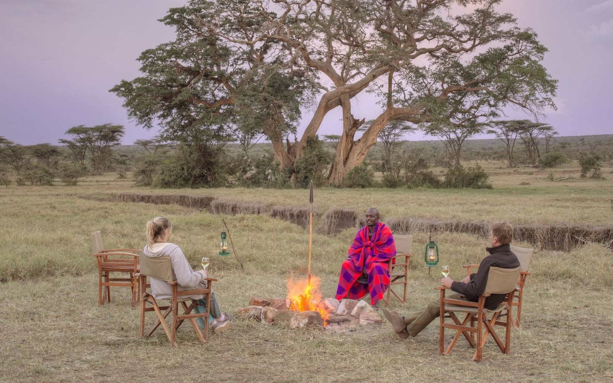 A couple sit with a local Maasai at Leopard Hill, Kenya.