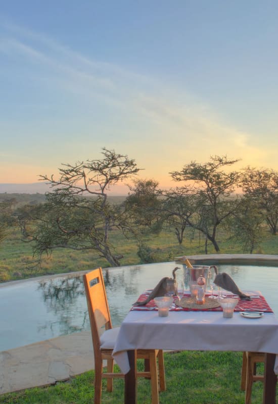A private dining experience is setup at the poolside during a gentle sunset.