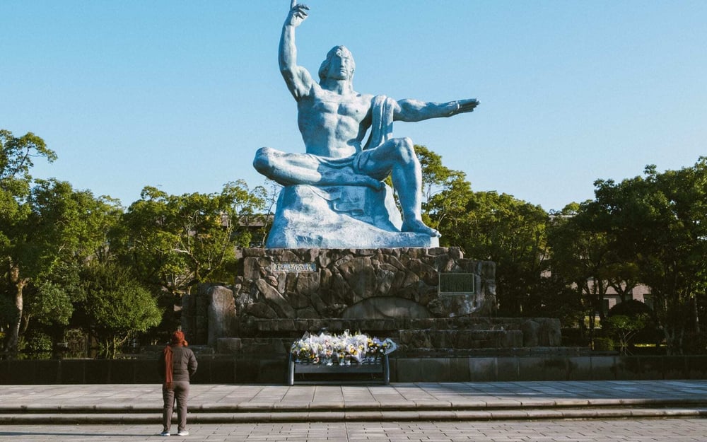A tourist gazes at the Peace statue in Nagasaki, Japan, a stone male figure.