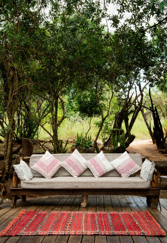 There is a wooden sofa chair dressed with comfy cushions and fronted by a hand-woven rug.