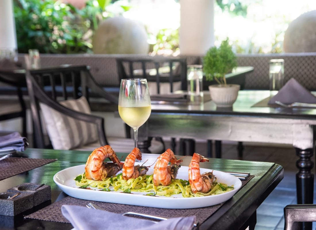 A dish of king prawns on a bed of vegetables is served beside a cold glass of white wine.
