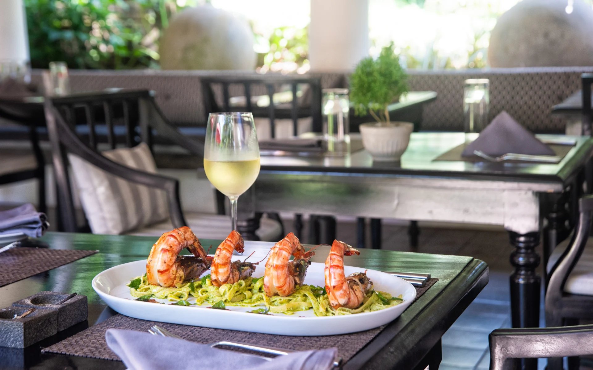 A table has a glass of white wine and a plate of shrimp. 