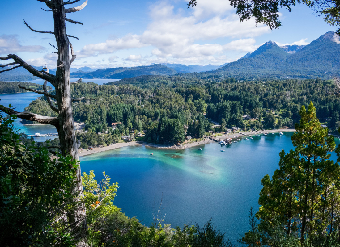 Standing on top of a mountain surrounded by trees is a viewpoint with the glistening blue lake at Villa La Angostura.