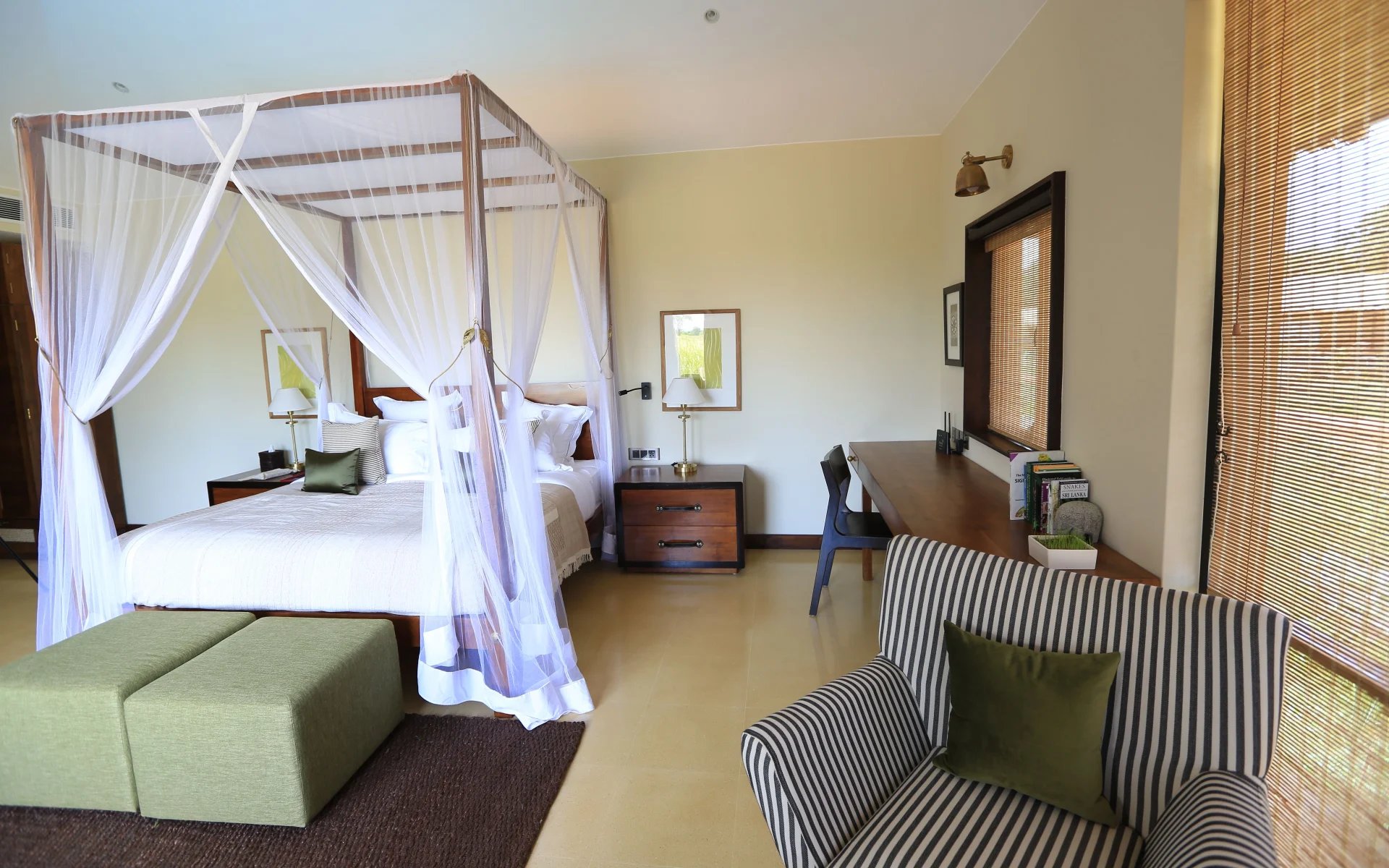 A four-poster bed is surrounded by an armchair and a writing desk. 