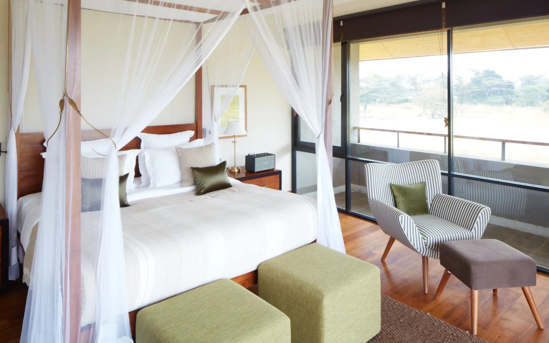 A four-poster bed is surrounded by an armchair and a writing desk. 