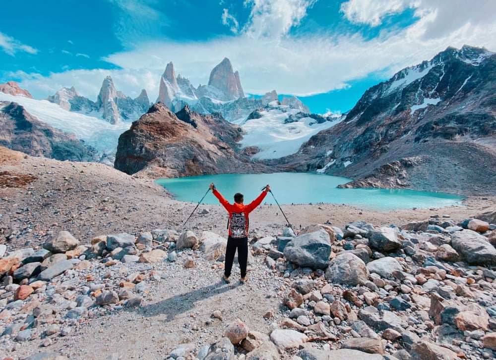 A hiker raises his walking sticks as he reaches the top of a snowy, Patagonian mountain.