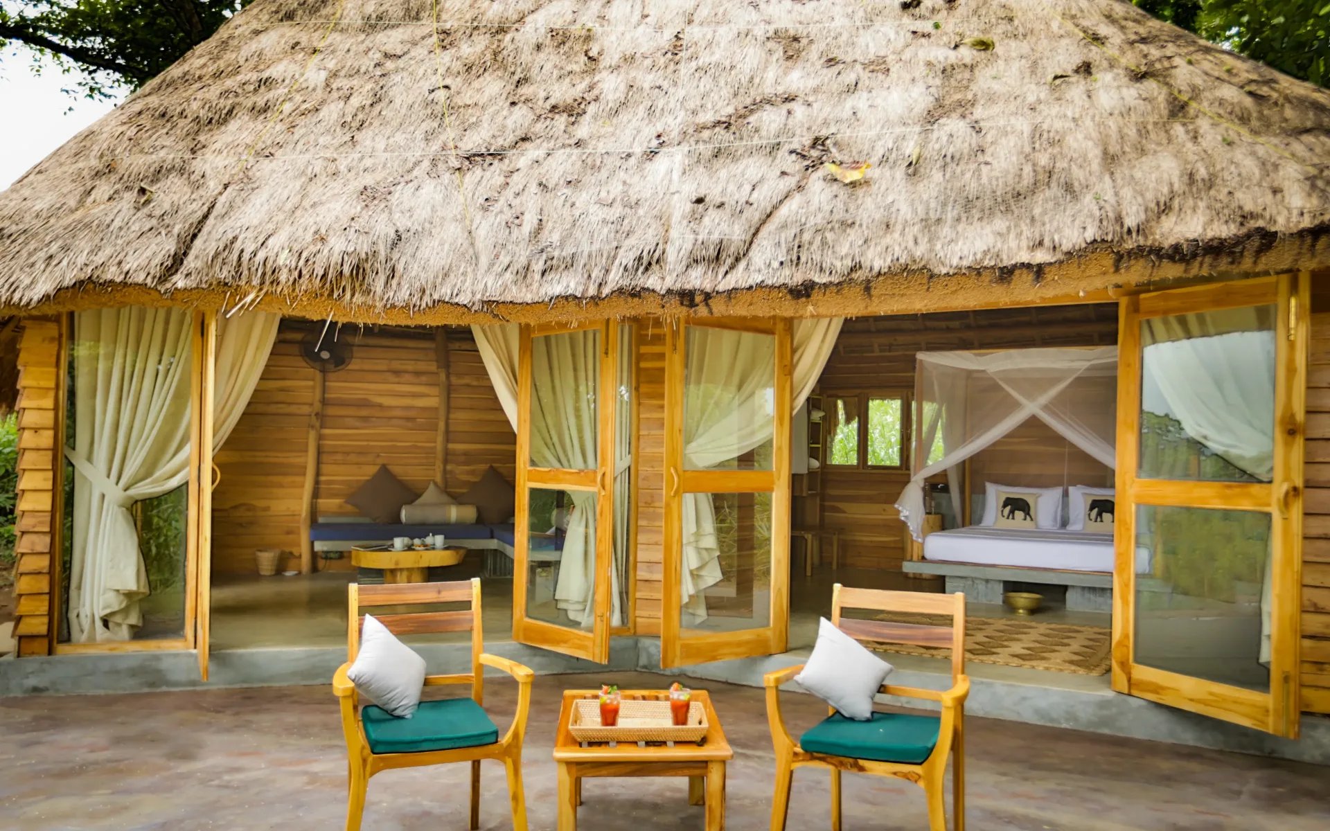 One of the bungalows at the lodge opens up onto a spacious veranda, where two wooden chairs are placed beside a table with two cocktails.