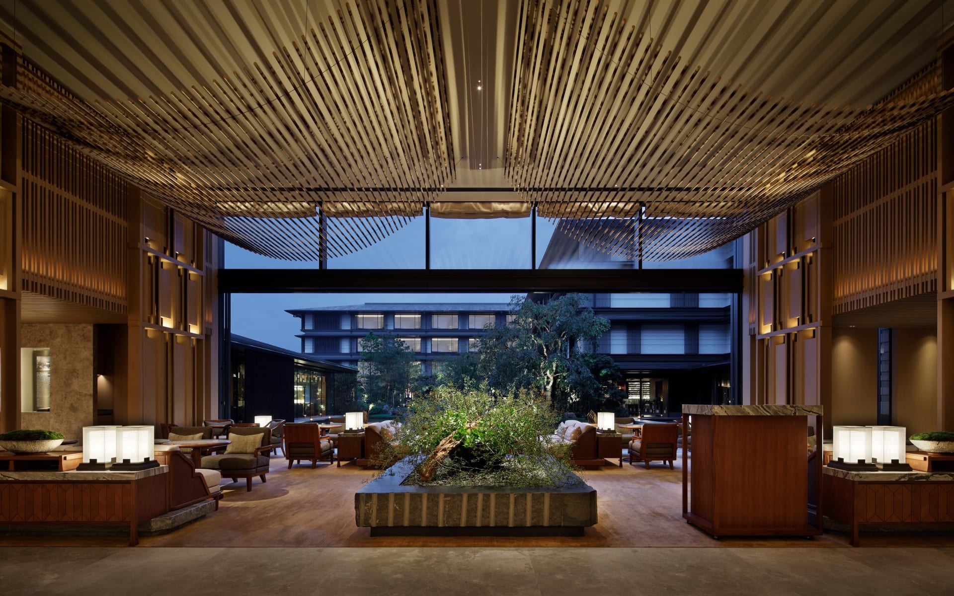 The lounge at The Mitsui in Kyoto has a high ceiling, lots of seating, open-floor plan and a plant in the middle of the room. 