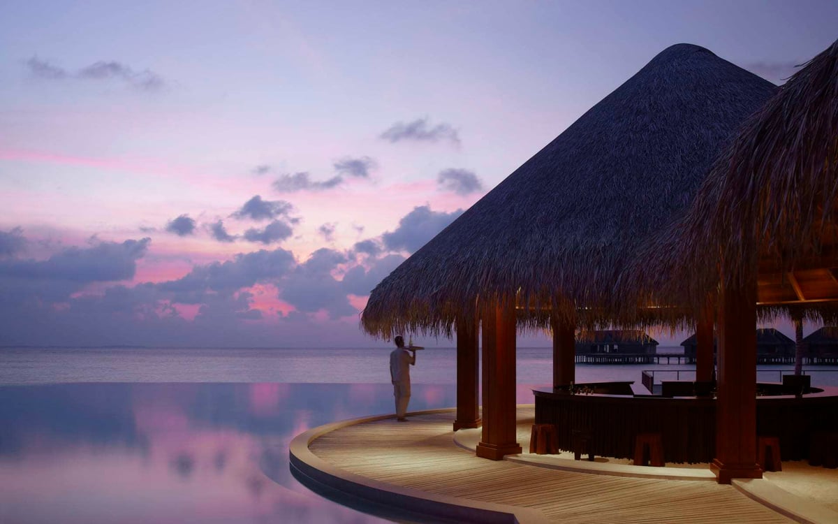 A server is at the bar at Dusit Thani Maldives at sunset.