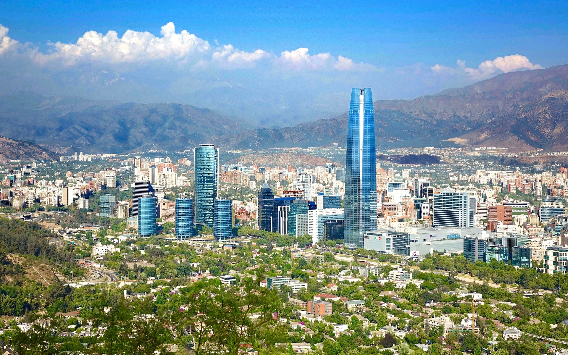 The city of Santiago in Central Chile is surrounded by mountains and interspersed with skyscrapers, clusters of buildings and trees. 
