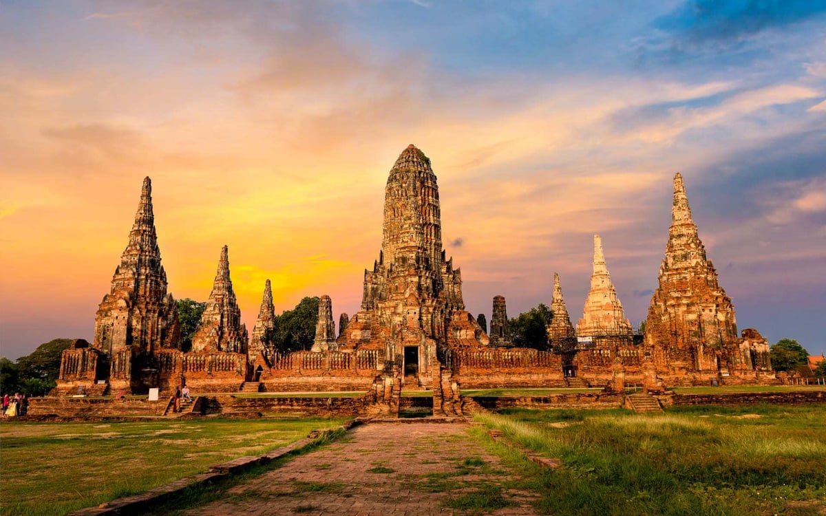 Wat Chaiwattanaram is a Buddhist temple in Thailand ahead of a yellow sunrise.