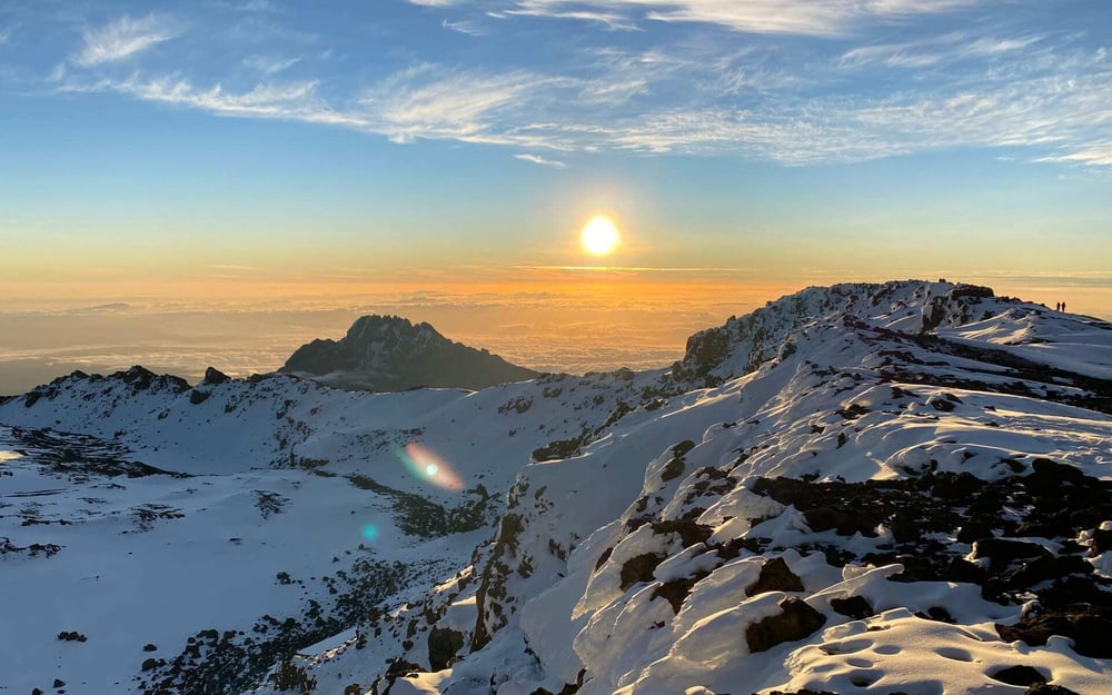 A high area of Mount Kilimanjaro is covered with snow during a yellow sunrise.