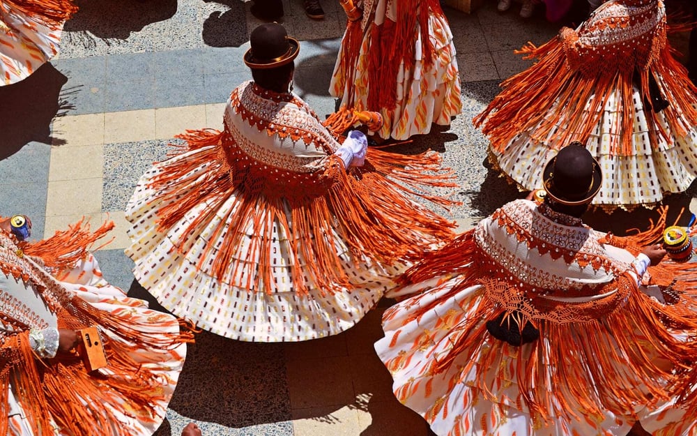 Dancers in Peru spin, wearing colourful, fringed orange skirts.