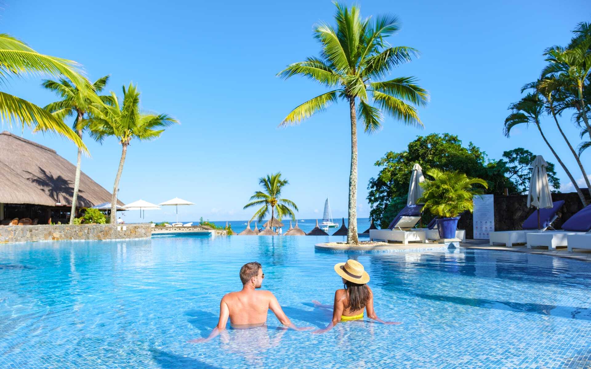 A couple enjoy a swimming pool in a tropical setting.