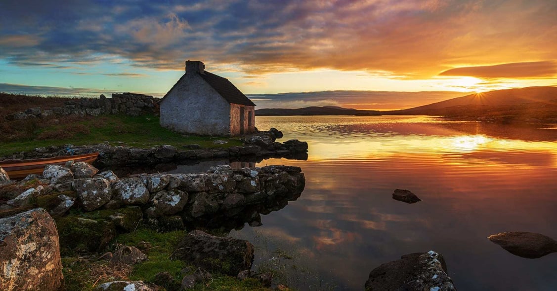 The sun sets over an old-fashioned cottage in Galway, Ireland.