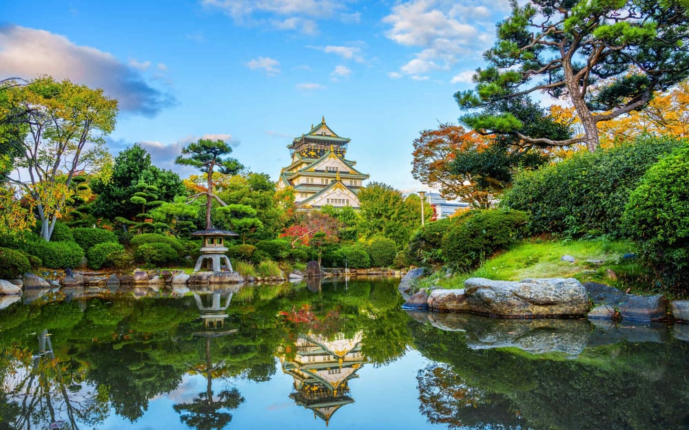 A traditional Japanese garden has a pond surrounded by foliage.