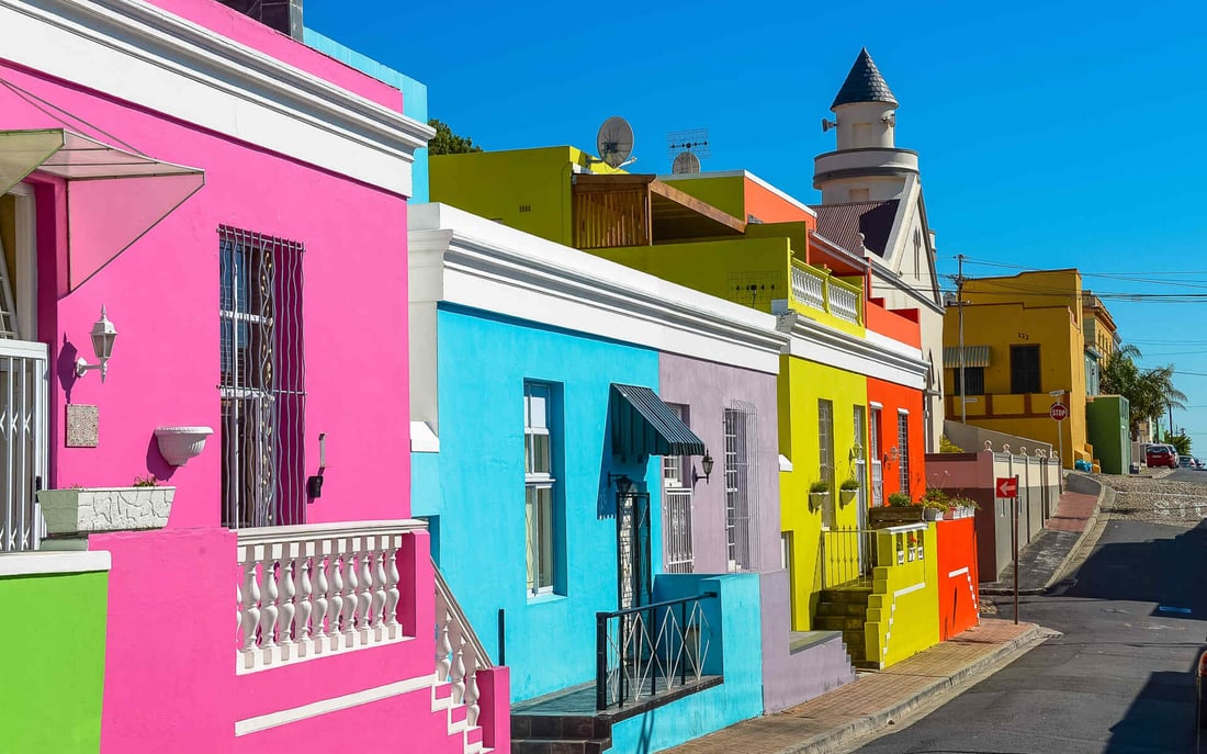 A row of pink, blue, yellow, and orange houses line a street in La Boca during daytime.