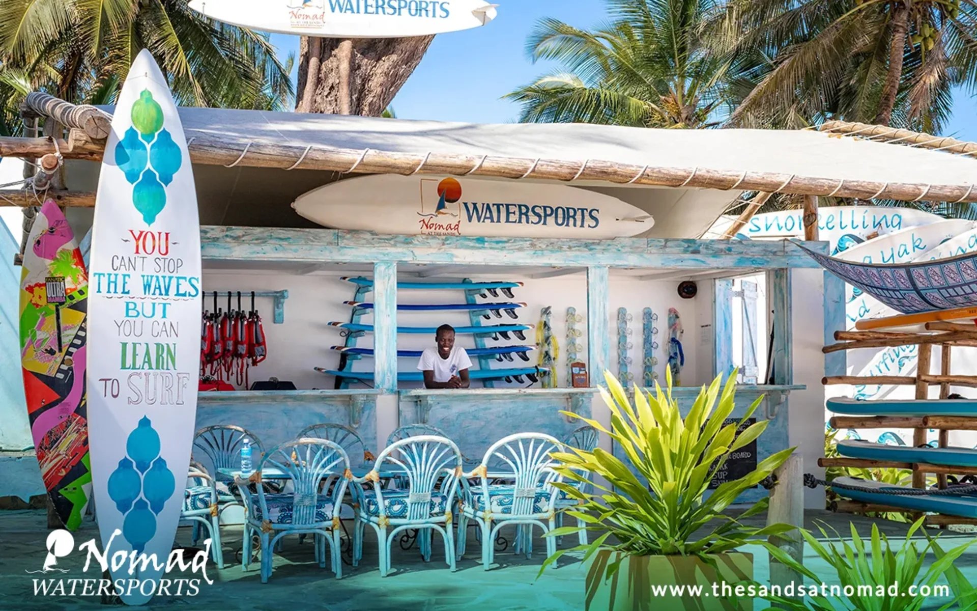 A man is standing at the front of an outdoor surf shop.