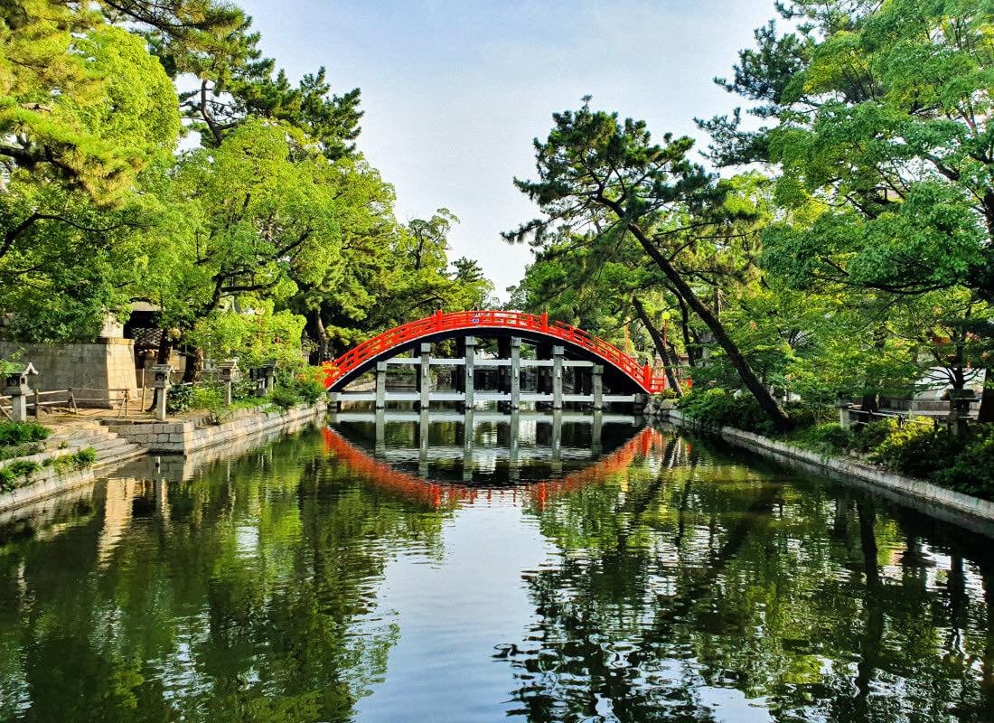A half-circle red bridge is reflected in a river in Osaka.
