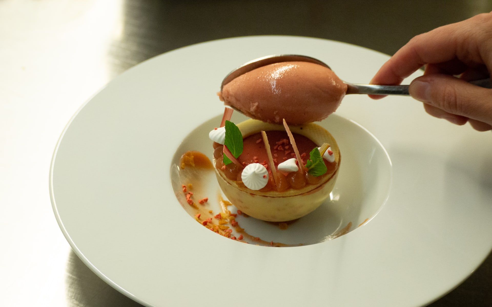 A person's hand is plating desert onto a bowl. 