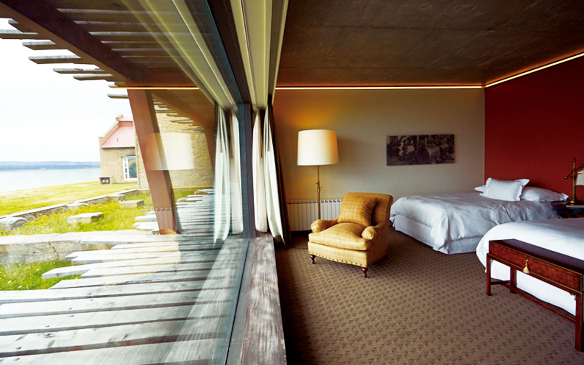 Twin beds and an armchair are positioned to look out of a rectangular-shaped, floor-to-ceiling window.
