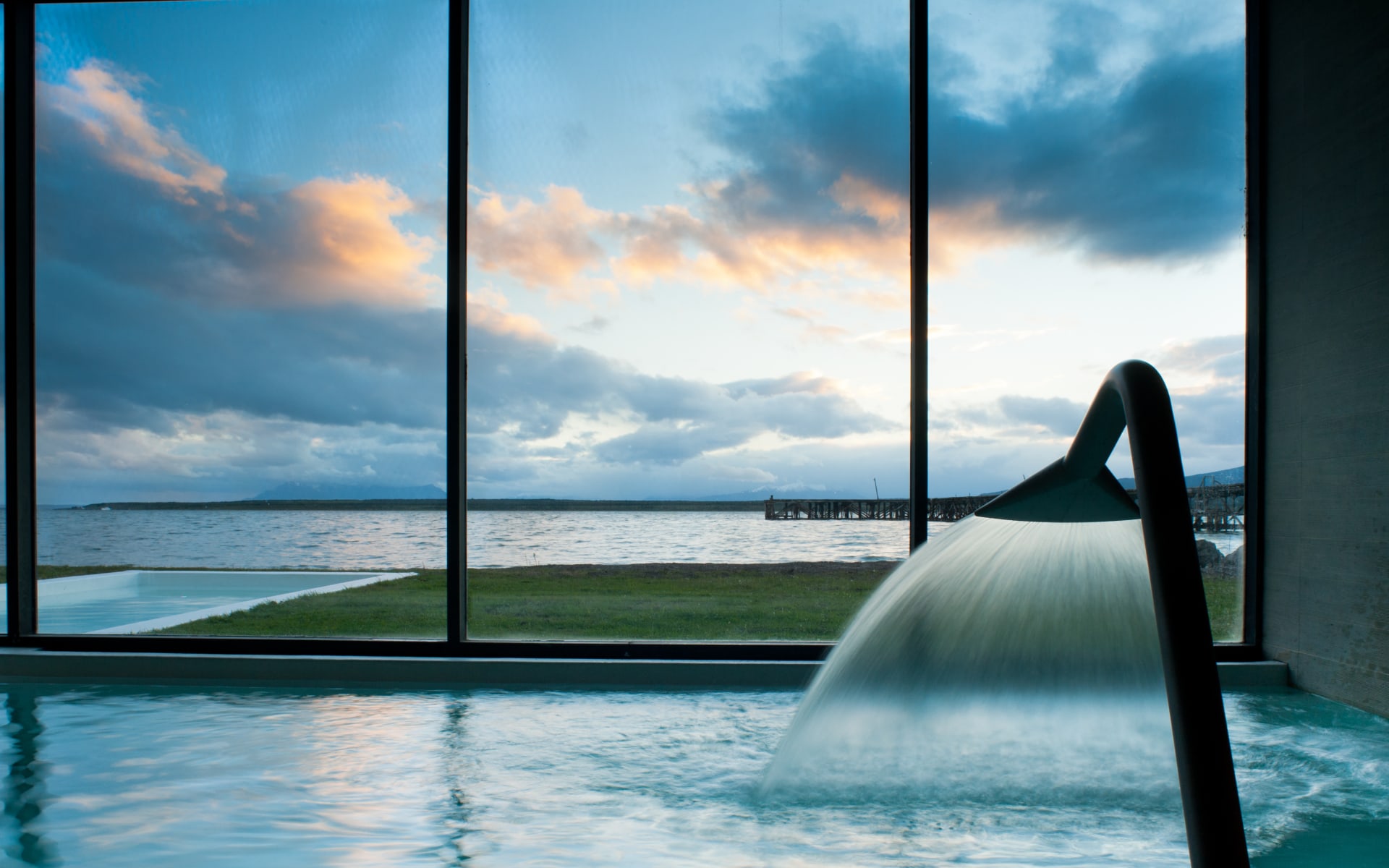 A pool overlooks floor-to-ceiling glass windows that reveal the sea. 