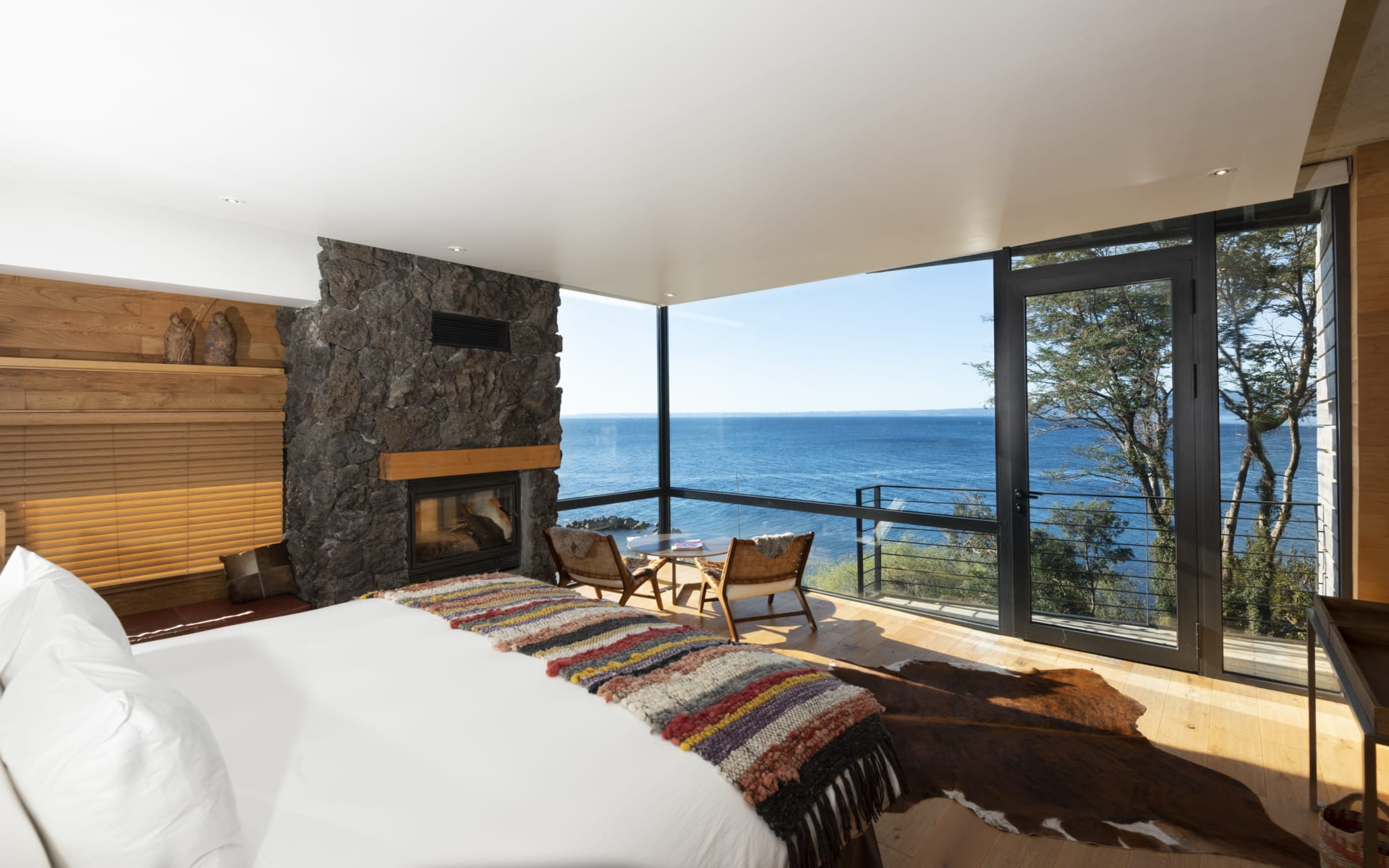 A large bed overlooks a balcony and blue ocean.