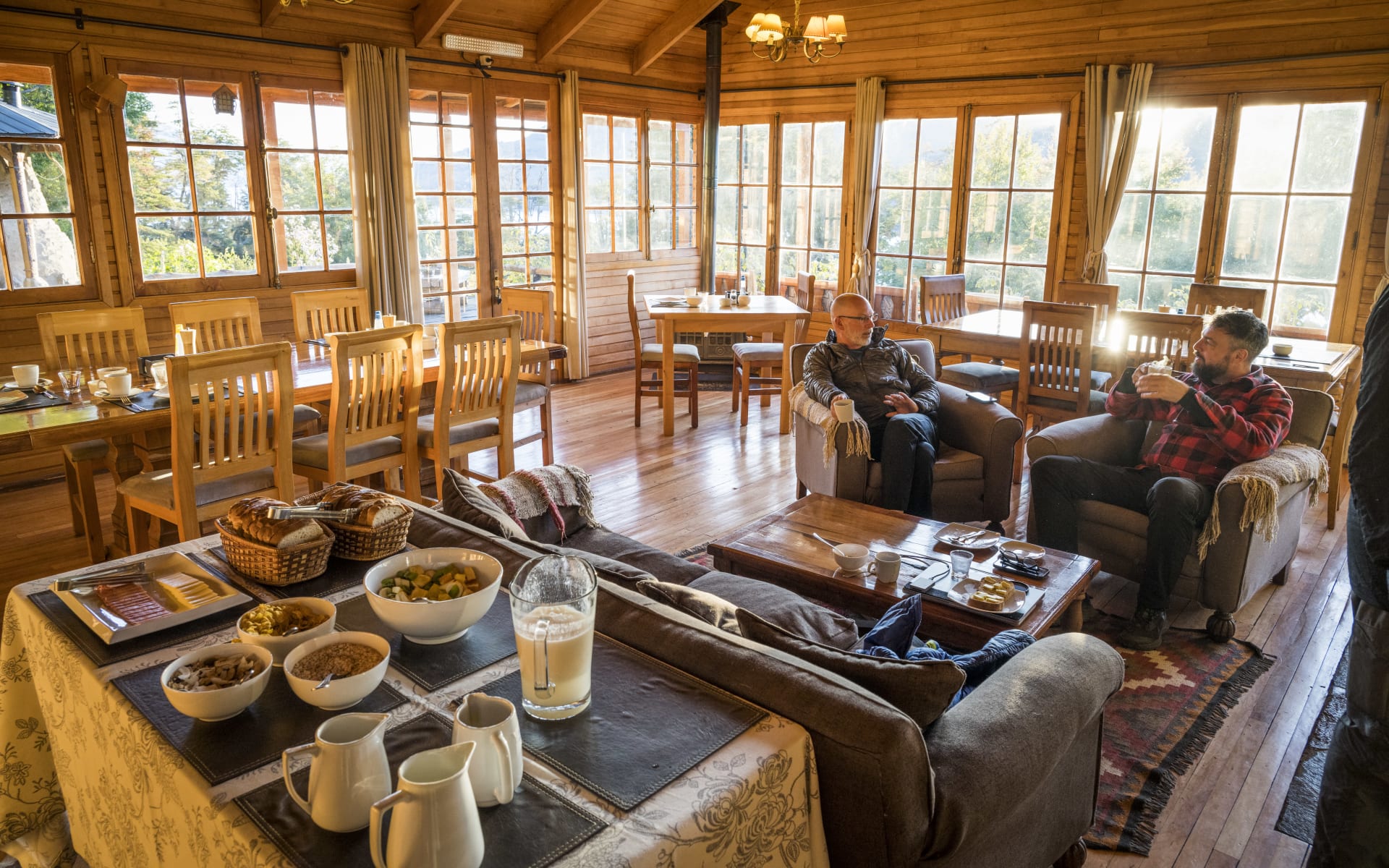 Two men sit on sofas in the lounge/dining area, enjoying breakfast and a hot drink. 