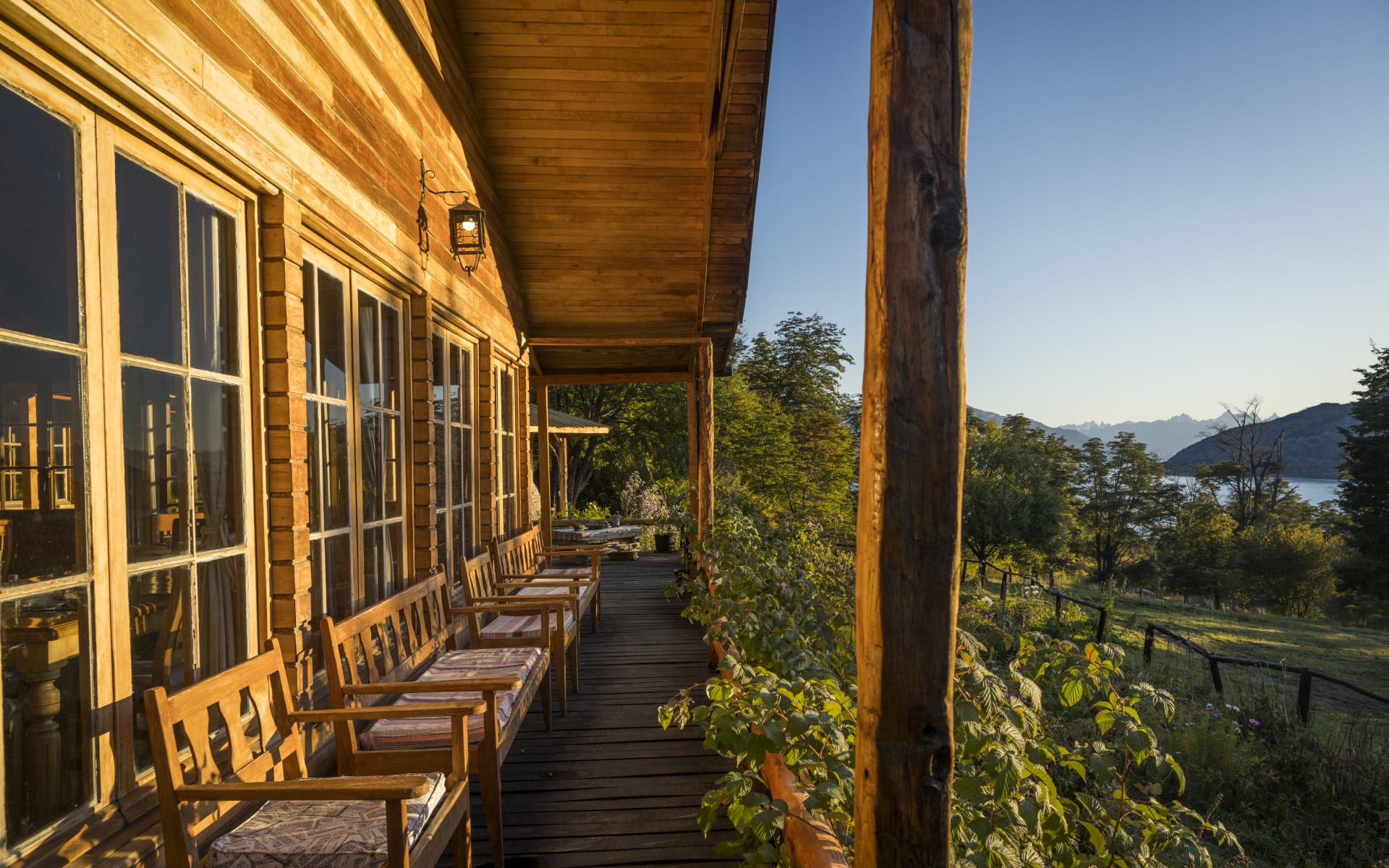 A wooden deck with chairs opens up to a green garden. 